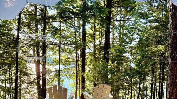 En træterrasse med Adirondack-stole, en hængekøje og udsigt til et skovområde.