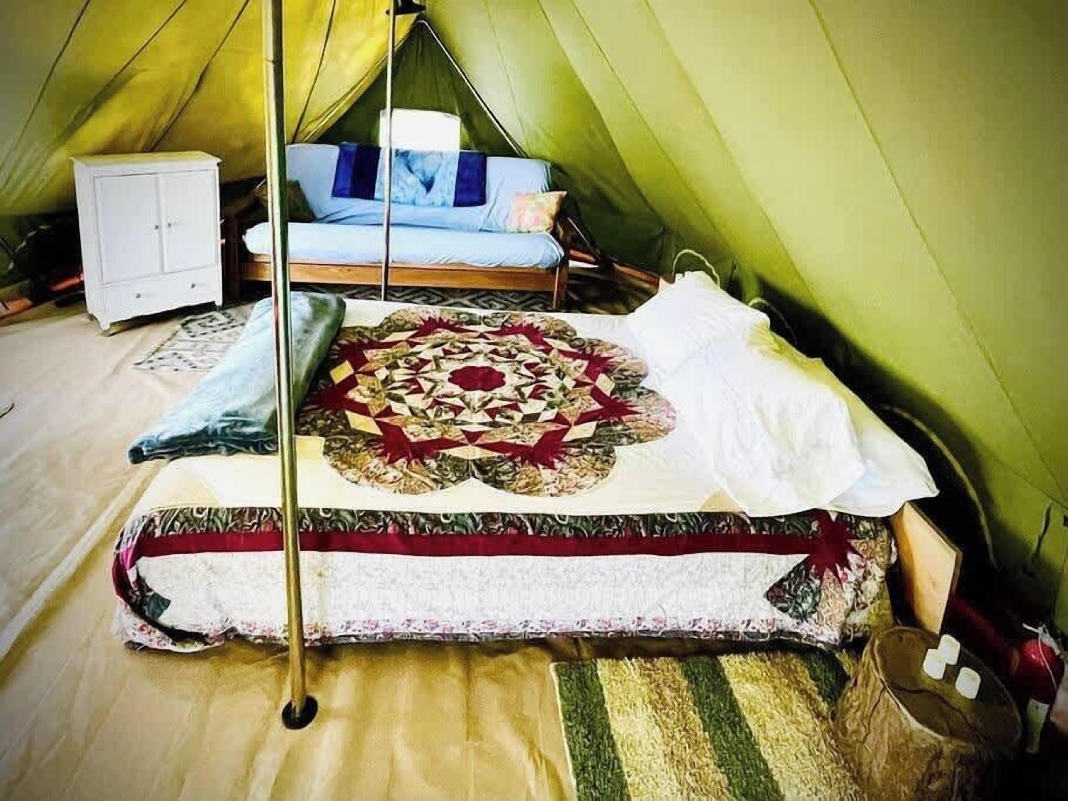 Een tent met een bed, een klein kastje en een decoratieve quilt.