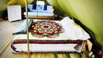 Een tent met een bed, een klein kastje en een decoratieve quilt.