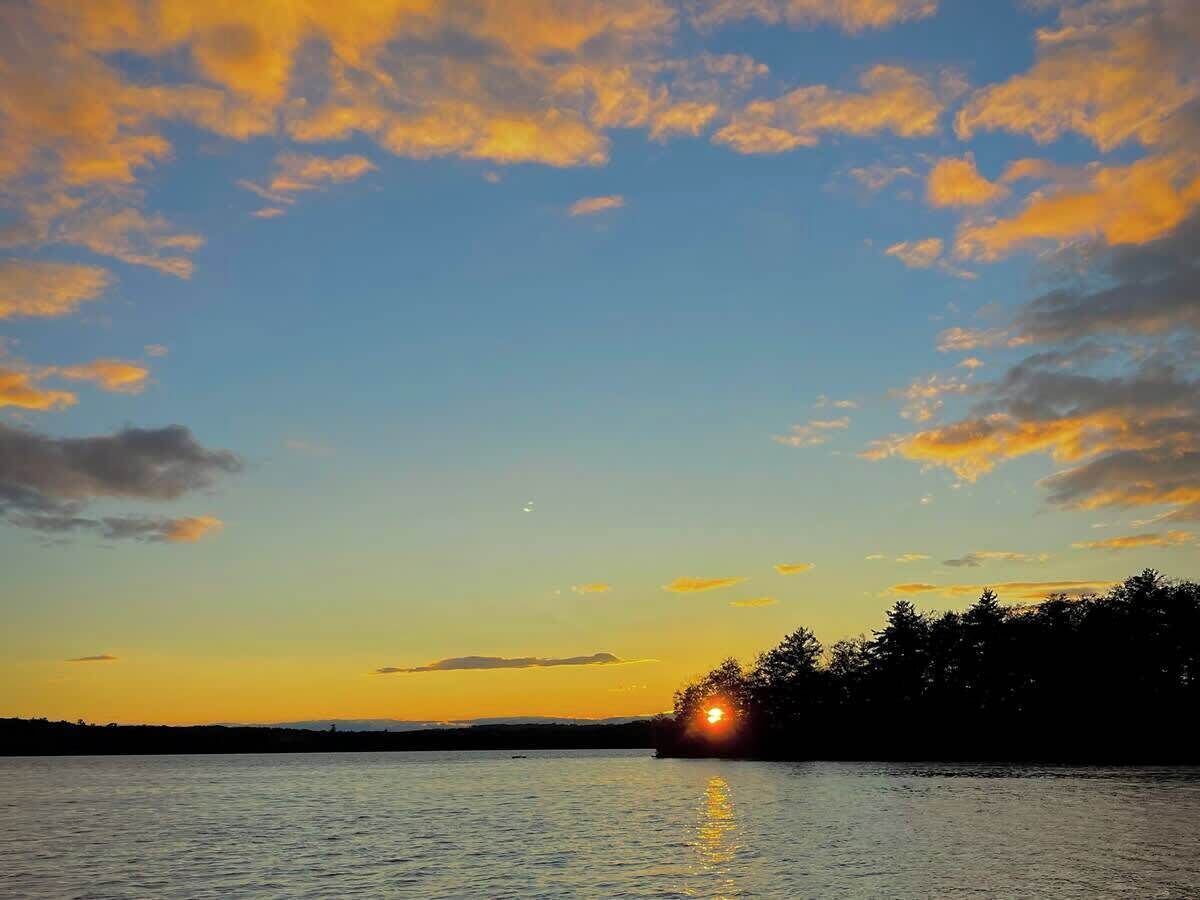 A sunset over a body of water with a silhouette of trees on the horizon.