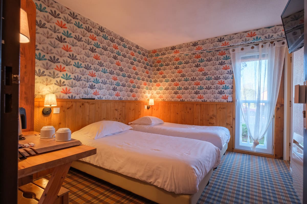 Ein Zimmer mit zwei Betten, einem hölzernen Kopfteil, einem Schachbrettfußboden und einer gemusterten Tapete.