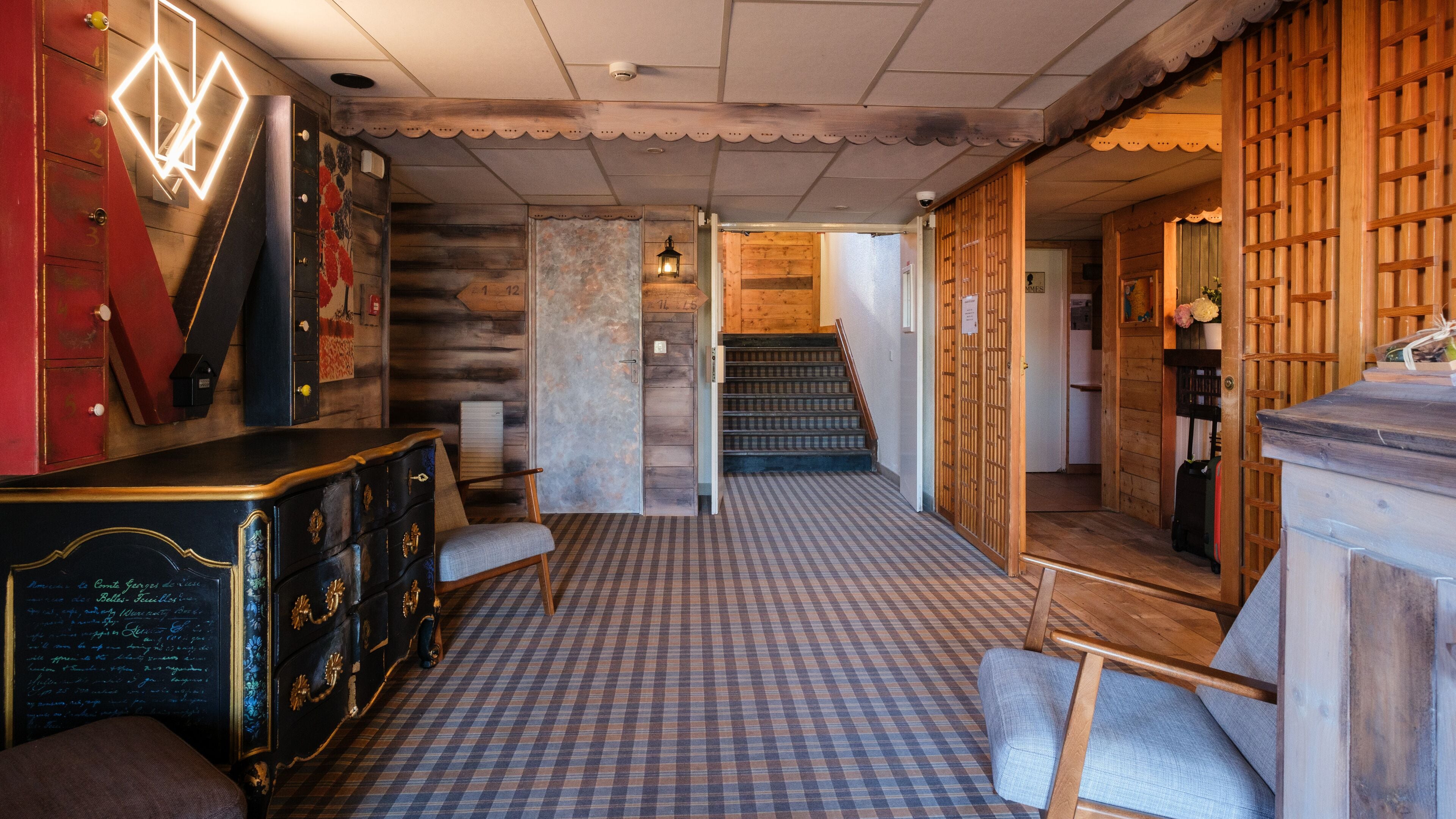 A hotel lobby with a checkered floor, a staircase, and a wooden reception desk.