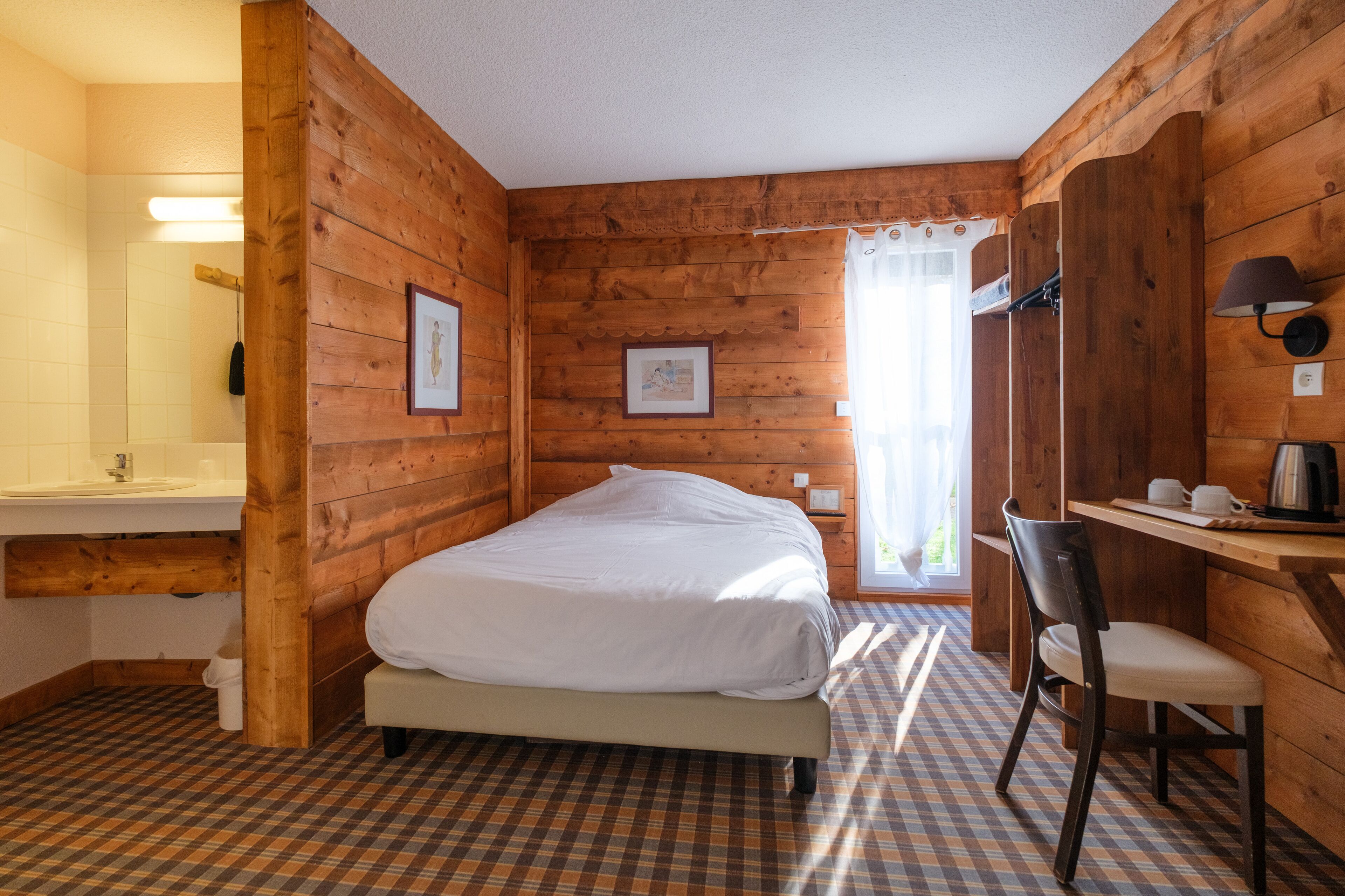 A wooden cabin room with a bed, a desk, and a chair.
