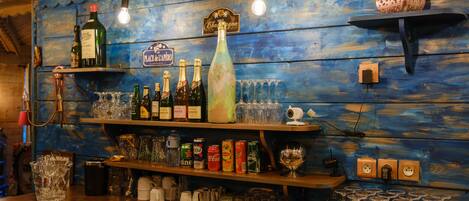 Zona de bar con estantes llenos de botellas, vasos y diferentes utensilios.