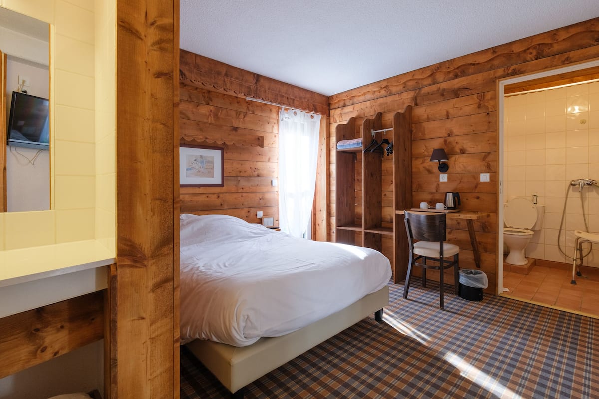 Ein Zimmer mit Holzboden, einem Bett, einem Sessel, einem kleinen Tisch und einem Badezimmer mit Toilette und Dusche.