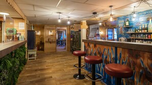 Een bar met houten vloer, barstoelen en diverse flessen en glazen op planken.