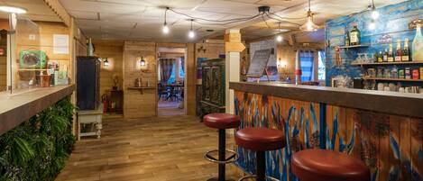 A bar area with wooden flooring, bar stools, and a variety of bottles and glasses on shelves.