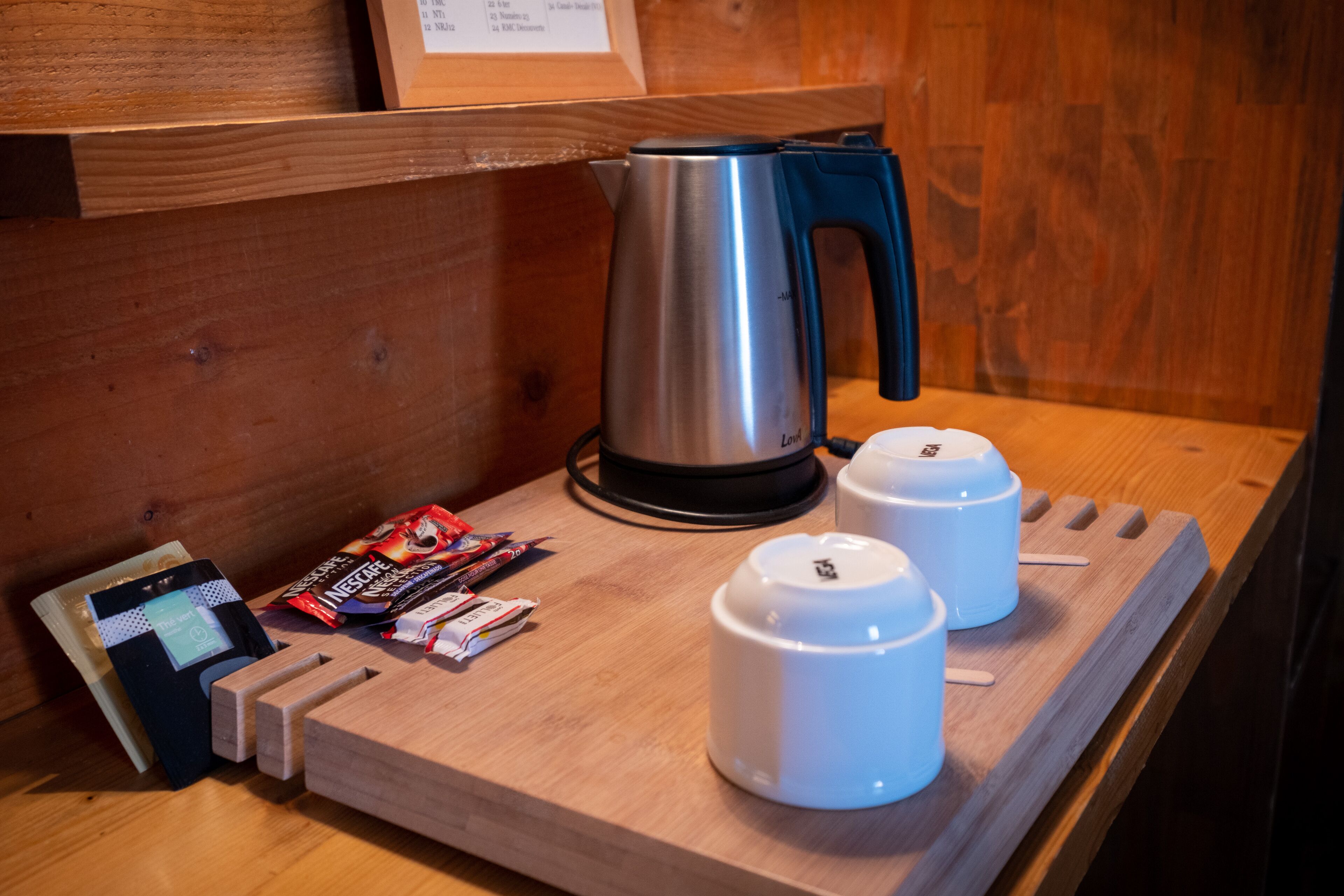 Una mesa de madera con un hervidor, dos tazas blancas, una cafetera y algunos paquetes de café.