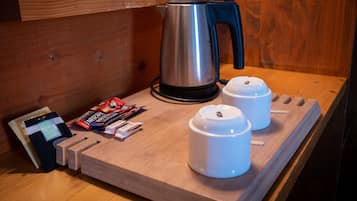 Une table en bois avec une bouilloire, deux tasses blanches, une machine à café et quelques sachets de café.