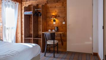 A wooden room with a bed, a chair, a desk with a lamp, and a wardrobe.