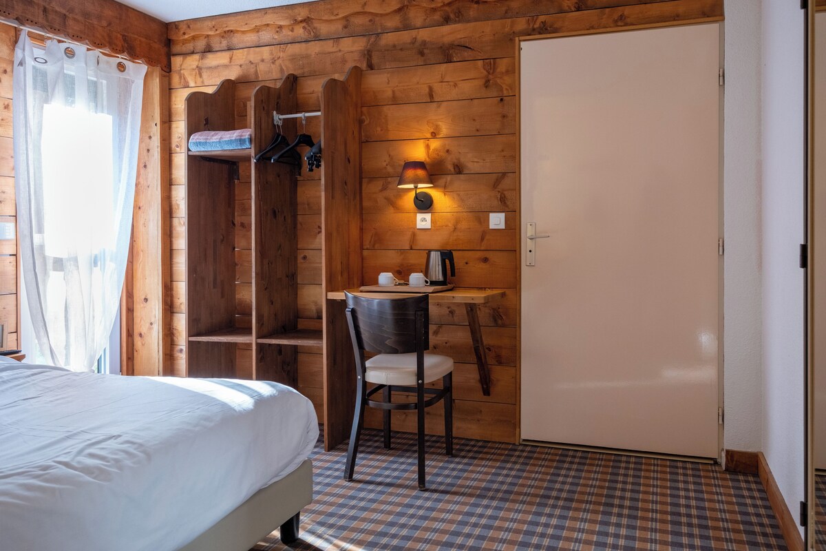 Een houten kamer met een bed, een stoel, een bureau met een lamp en een kledingkast.