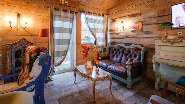 Een gezellig interieur van een houten blokhut met een leren bank, een vintage blauwe fauteuil, een houten kast en een televisie aan de muur.