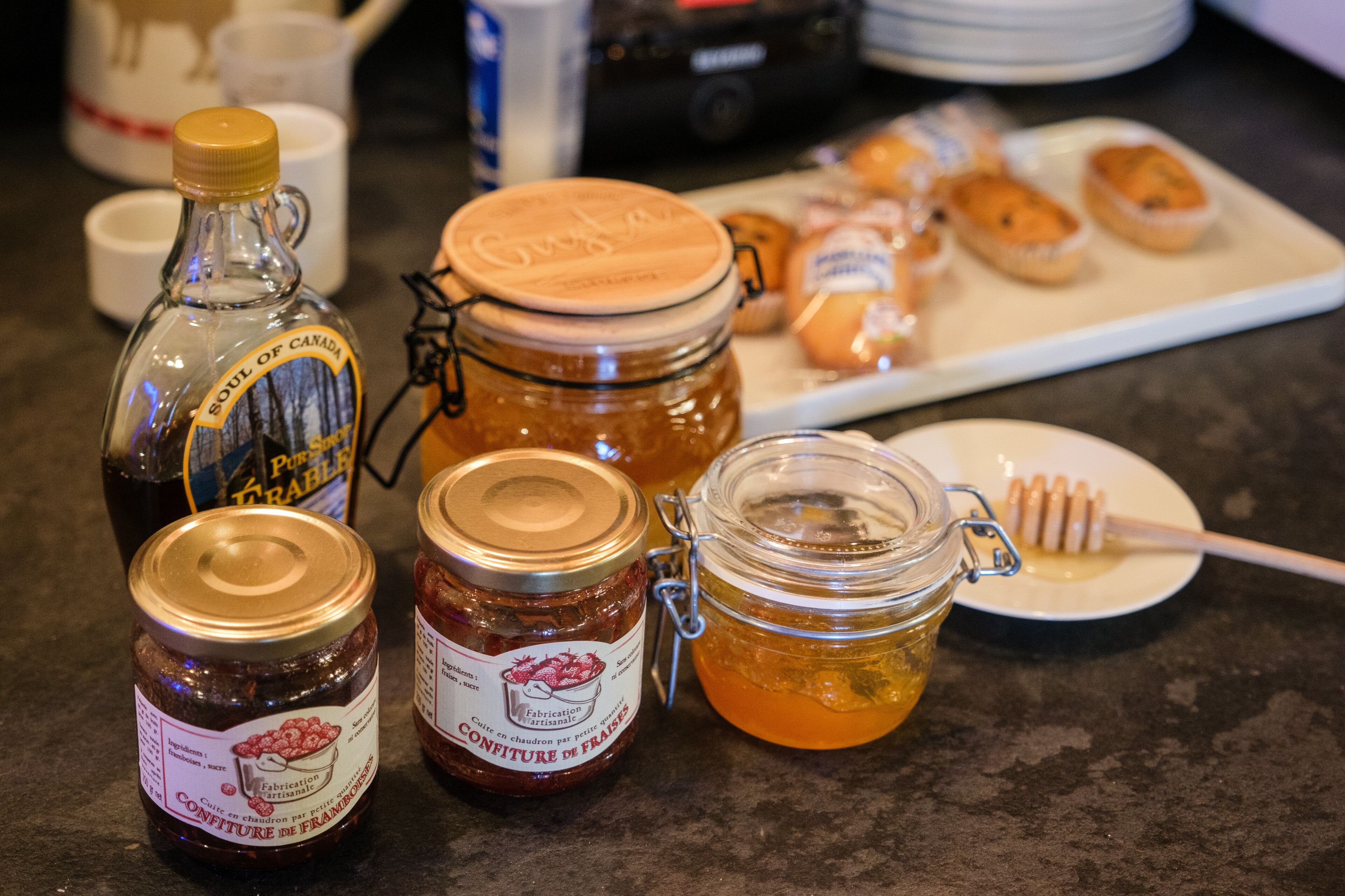 A table with various food items including jars of honey and jam, a honey dipper, and pastries.