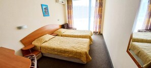 A hotel room with two single beds, a wooden headboard, a small table, and a picture on the wall.