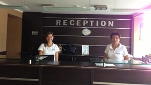 A reception desk with a sign that reads 'RECEPTION' above it. There is a clock on the wall and a framed certificate or award hanging on the wall. - Hotel Pliska (Nessebar)