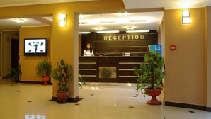 A reception area with a reception desk, potted plants, and a television screen. - Hotel Pliska (Nessebar)