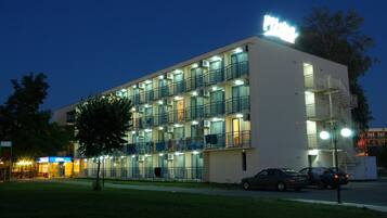 A multi-story hotel with balconies, a visible fire escape, and a parking area with cars.