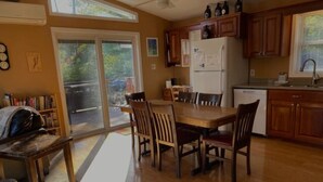 A kitchen with wooden cabinets, a dining table with chairs, a refrigerator, and a window overlooking a backyard.