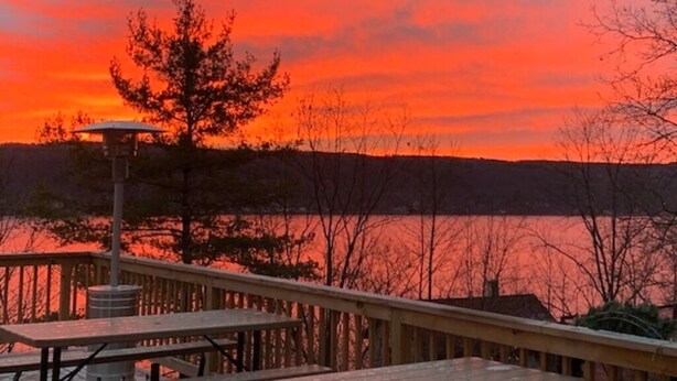 A wooden deck with a metal railing overlooking a body of water during sunset.