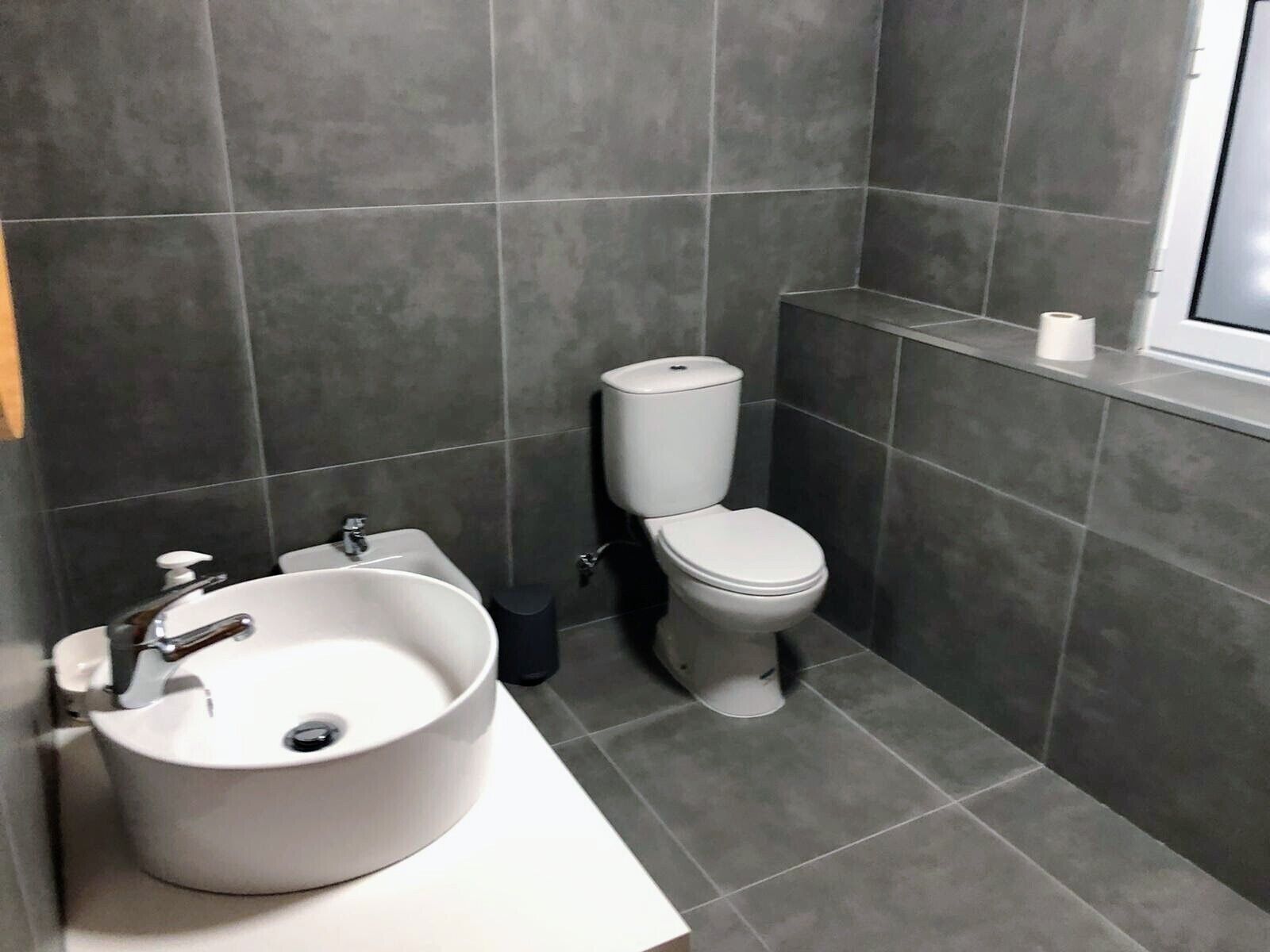 A modern bathroom with a large sink, toilet, and a window above the toilet.