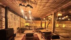 A cozy restaurant with stone walls, wooden ceiling, and large windows. Tables and chairs are arranged for dining.