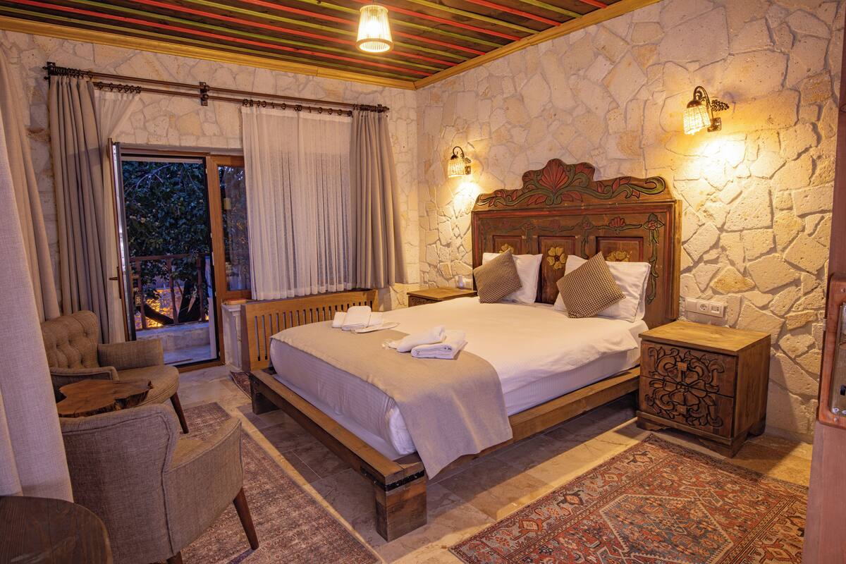 A bedroom with a stone wall, a wooden bed, a nightstand, a chair, and a view through a glass door.