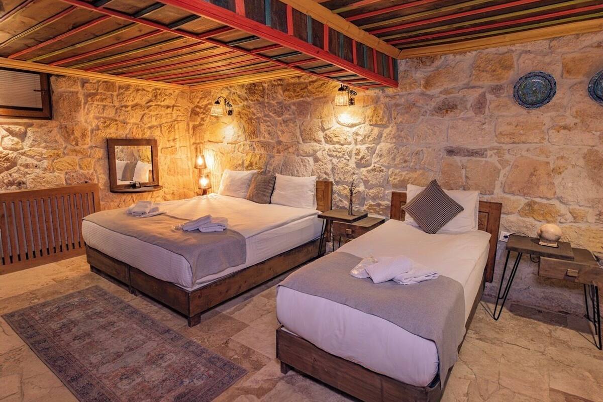 A room with two beds, stone walls, and a wooden ceiling.