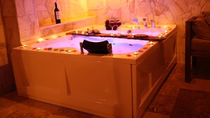 A spa bath with candles, a bottle of wine, and two glasses of red wine.