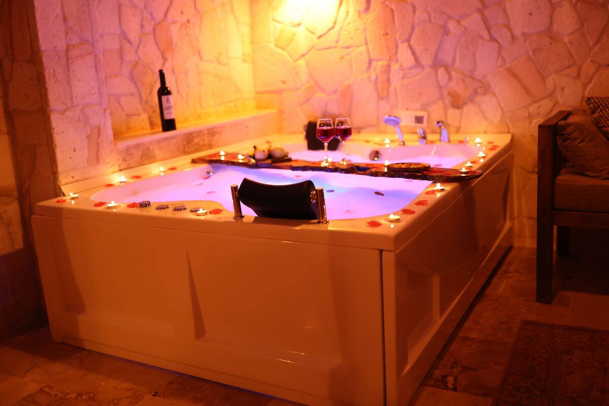 A spa bath with candles, a bottle of wine, and two glasses of red wine.