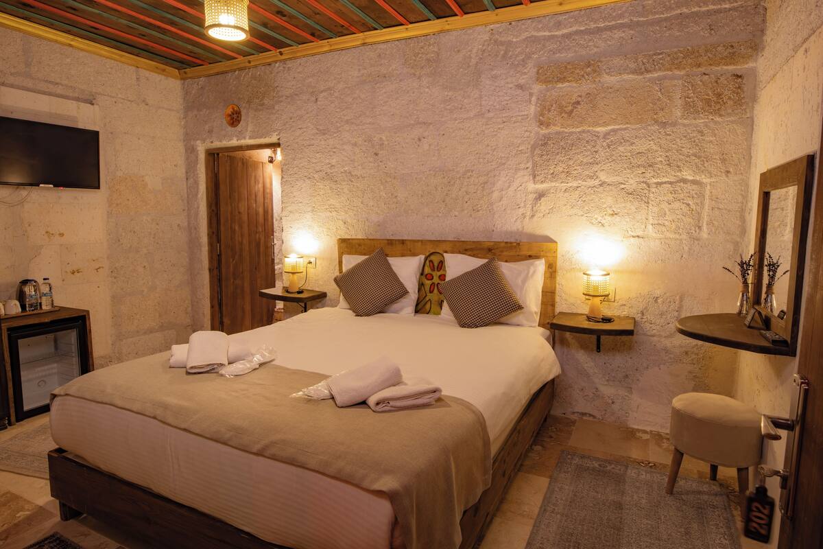 A well-lit bedroom with a large bed, wooden headboard, and bedside tables with lamps.
