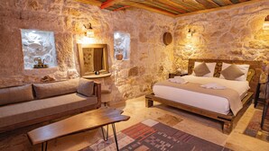 A stone-walled bedroom with a bed, a sofa, a bench, and a rug. - Casa Di Cappadocia (Nevsehir)