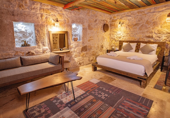 Un dormitorio con paredes de piedra, una cama, un sofá, un banco y una alfombra.