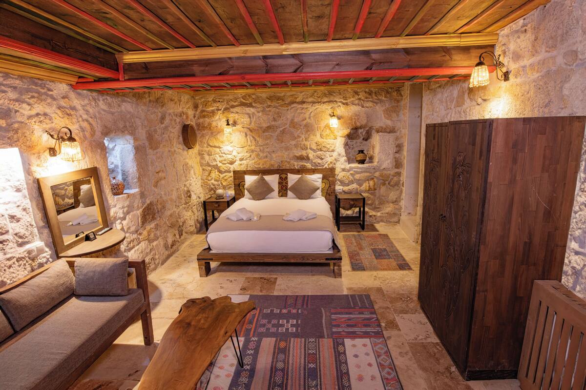 A rustic bedroom with a stone wall, wooden ceiling, and a bed with pillows.