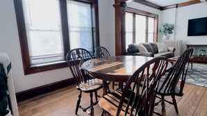 Un comedor con una mesa y sillas de madera, ventanas amplias y un ventilador de techo.
