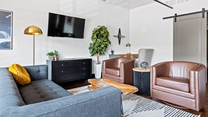 A modern living room with a grey sofa, two brown leather armchairs, a black entertainment unit, a large flat-screen TV, and a potted plant. - The Badlands Loft  (Rapid City)