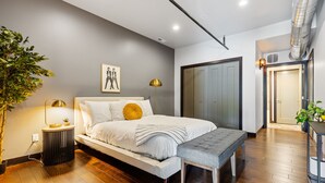A modern bedroom with a large bed, bedside lamps, a bench, and a potted plant. - The Badlands Loft  (Rapid City)