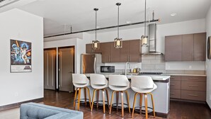 A modern kitchen with stainless steel appliances, wooden bar stools, and pendant lighting. - The Badlands Loft  (Rapid City)