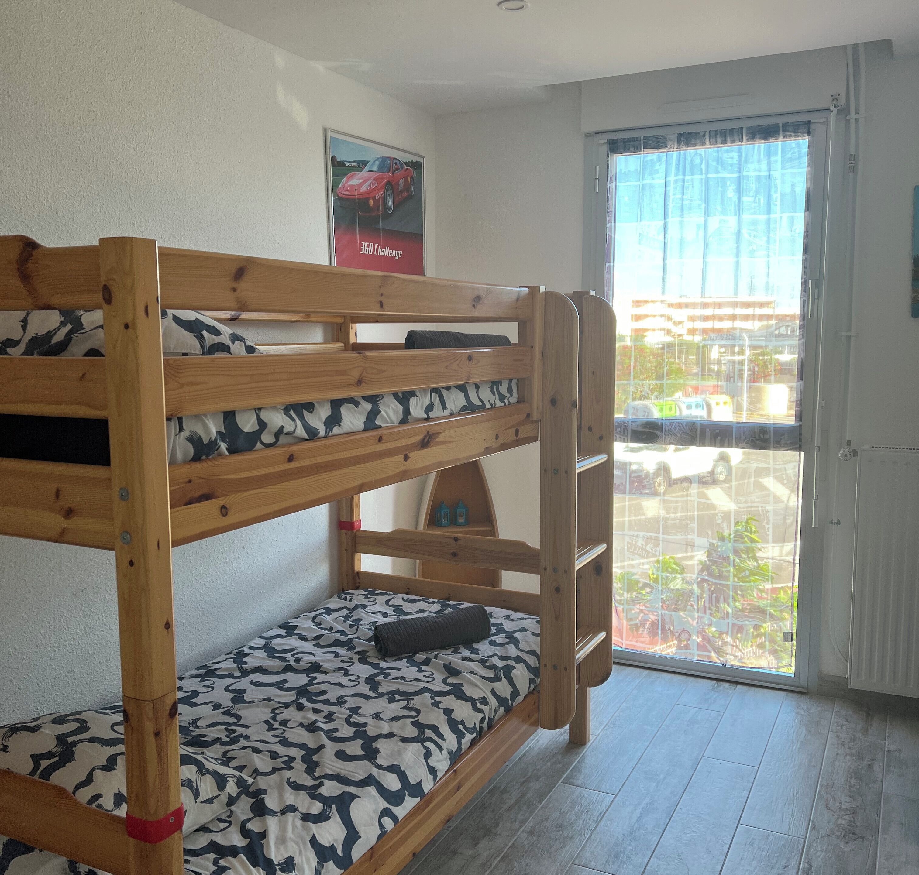 Ein Stockbett mit gemusterten Betttextilien, ein Poster an der Wand und ein Blick durch eine Glastür.