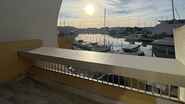 A balcony with a view of a marina and boats, a clear sky, and the sun setting or rising.