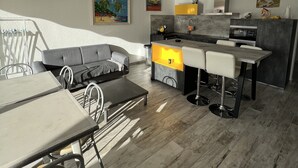 A modern living room with a grey sofa, a dining table with chairs, and a kitchen area with a bar counter.