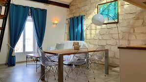 A dining area with a wooden table and chairs, a stone wall, and a window with curtains.