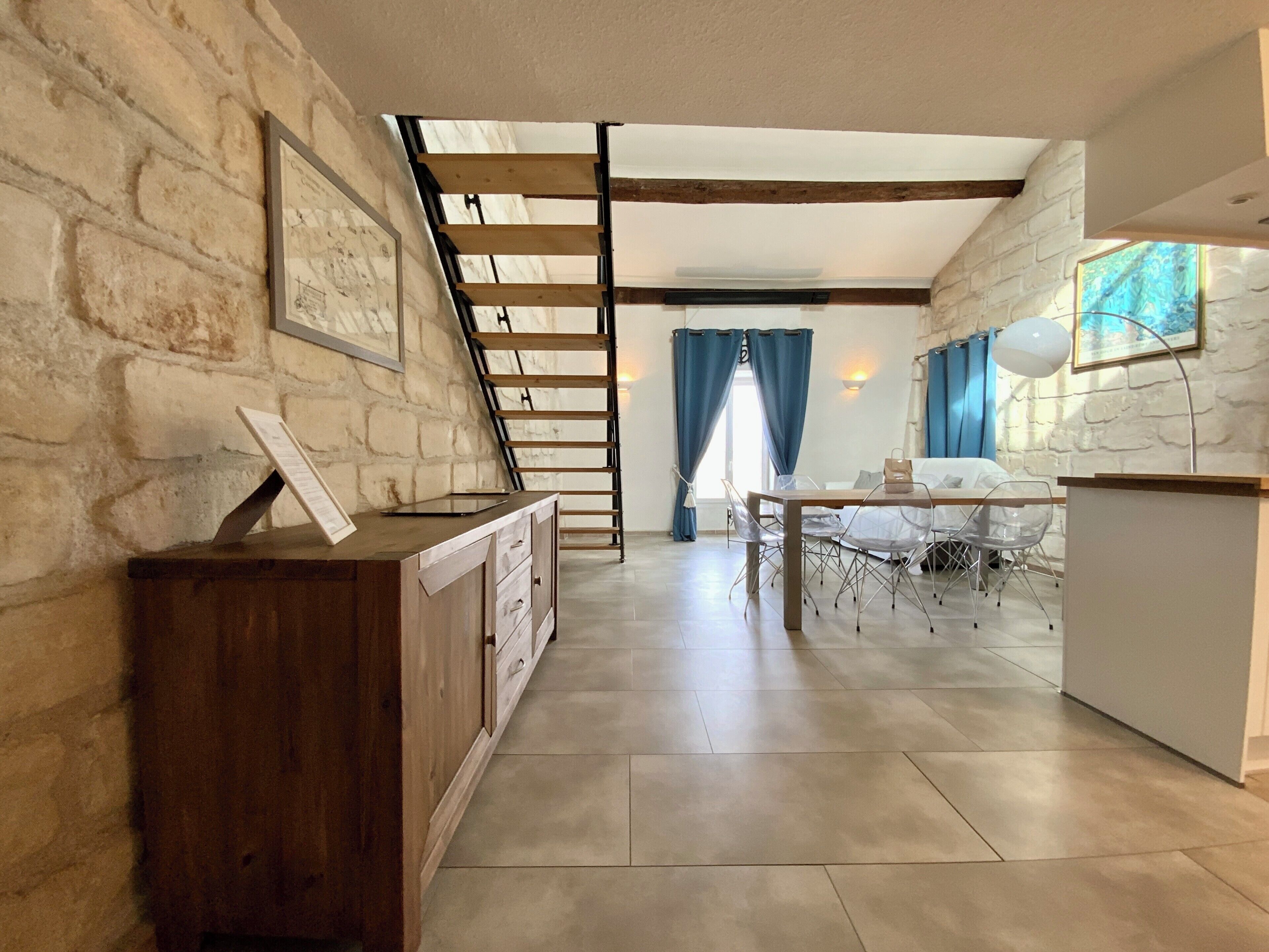 Ein geräumiger Raum mit hoher Decke, einer Holztreppe, einem Essbereich mit Tisch und Stühlen sowie einer Tafel an der Wand.