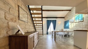 A spacious room with a high ceiling, a wooden staircase, a dining area with a table and chairs, and a whiteboard on the wall.