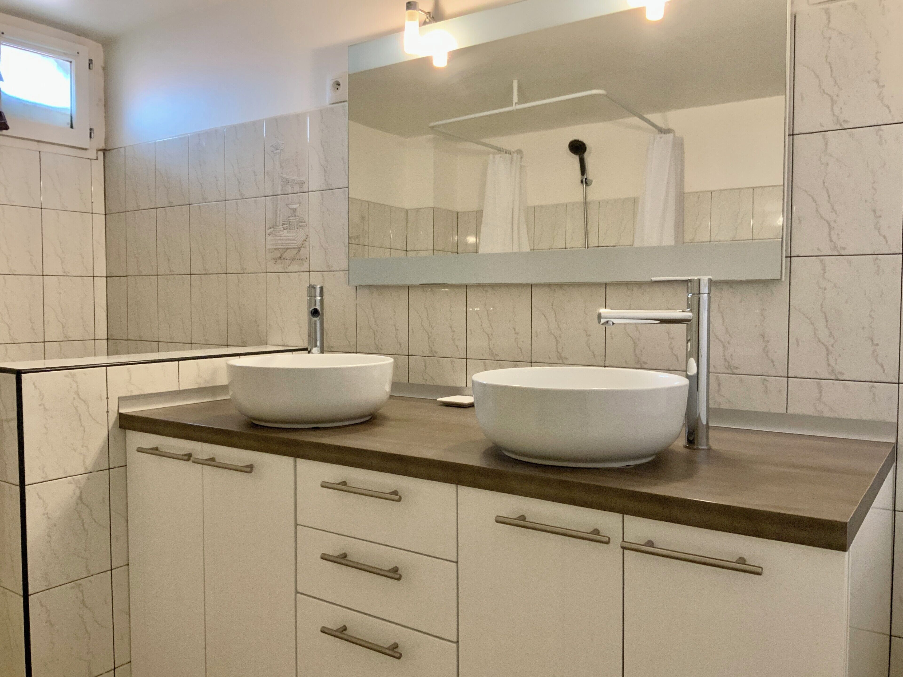 Ein modernes Badezimmer mit zwei großzügigen Waschtiegeln, einem großen Spiegel und einer Dusche.