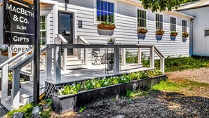Un bâtiment blanc avec un porche, une enseigne indiquant « MACBETH & CO. Cadeaux », et des jardinières remplies de fleurs placées sur les fenêtres.