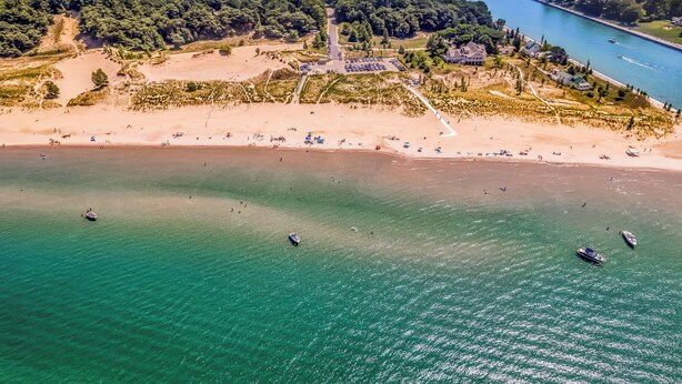 Vue aérienne d’une zone côtière avec une plage, un parking et une rangée de maisons le long du littoral.