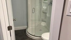Ein Badezimmer mit einer Duschkabine, einer Toilette und einem gefliesten Boden.