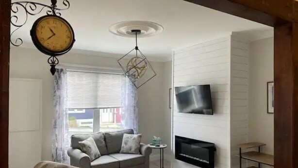 Ein Wohnzimmer mit Sofa, Sessel, Fernseher, Kamin und einer Uhr.