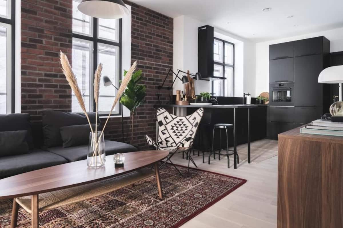 Un salon moderne avec un canapé foncé, une table basse en bois et un tapis à motifs.