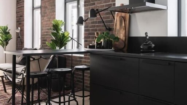A modern kitchen with a brick wall, black cabinets, and a large window. - Stay Bryggen - Serviced Apartments (Bergen)